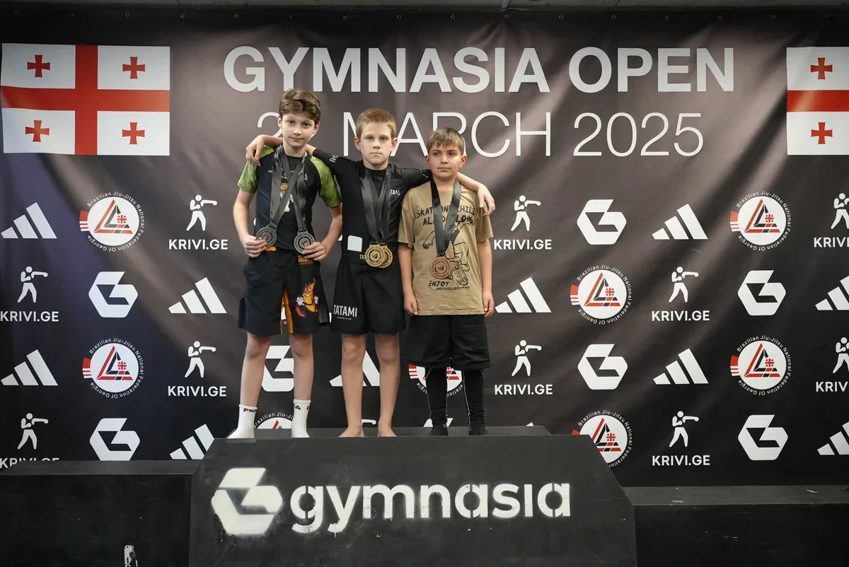 Three young medallists on the podium at Gymnasia Open, March 2025, under the Brazilian Jiu-Jitsu National Federation of Georgia banner